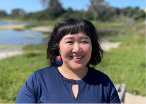 Céline, a woman with black hair wearing a navy blue blouse, stands in front of the UCSB lagoon.